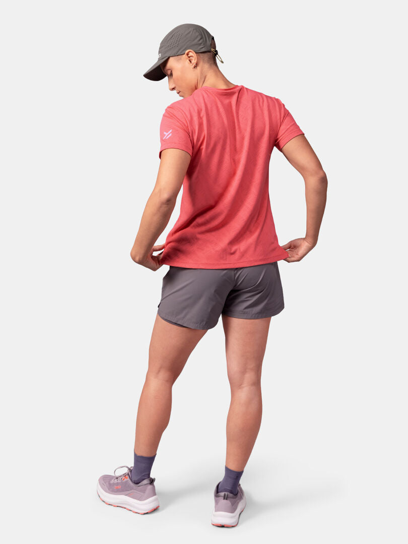 Person standing and facing away, wearing a Halti Oulanka T-shirt Women's, gray shorts, gray cap, purple socks, and pink sneakers.