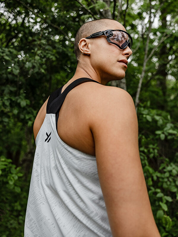 A person in the Halti Oulanka Training Top Women's wears goggles and stands outdoors in a wooded area, looking back.
