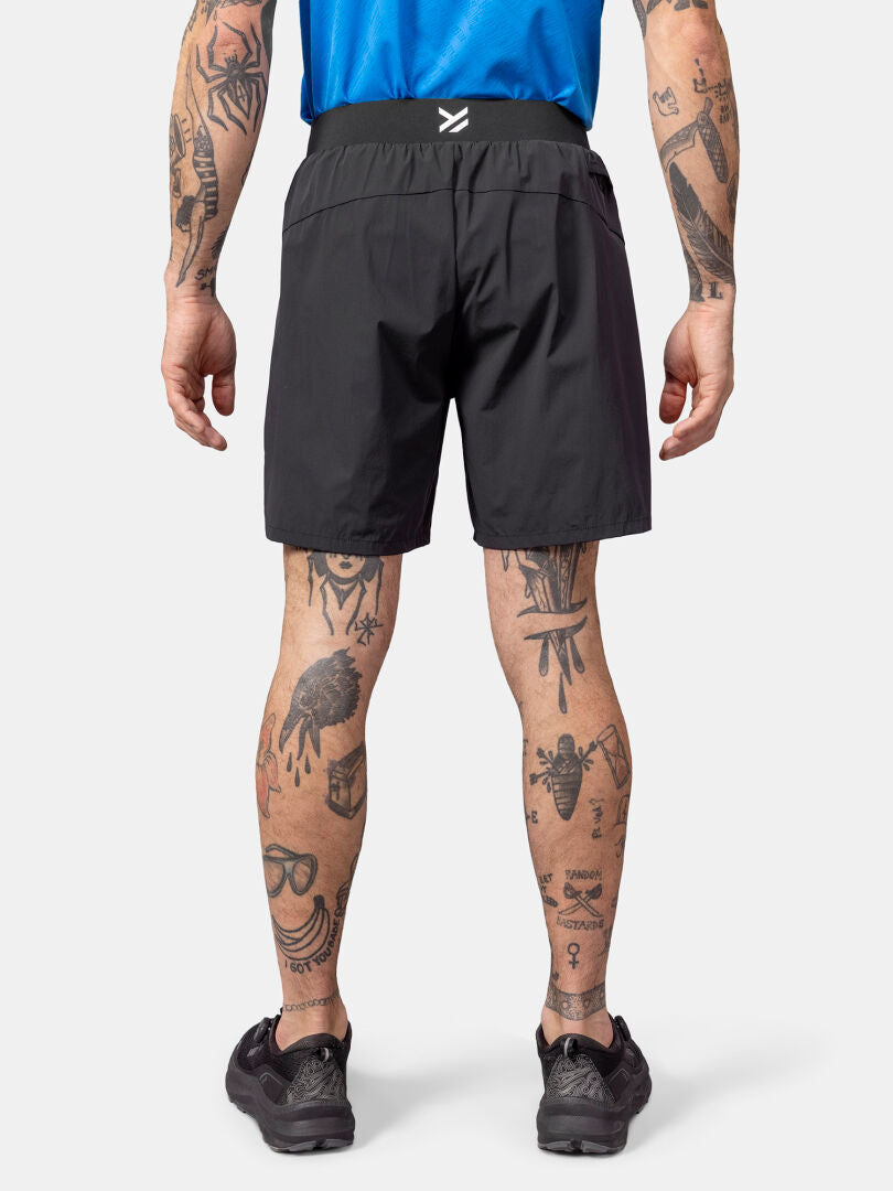 A person in Halti Uurto Shorts Men's and black shoes, shown from the back, with tattooed legs and arms.