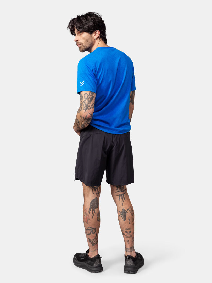 Man with tattoos in a Halti Oulanka T-shirt, blue, black shorts, and sneakers stands with his back to the camera.