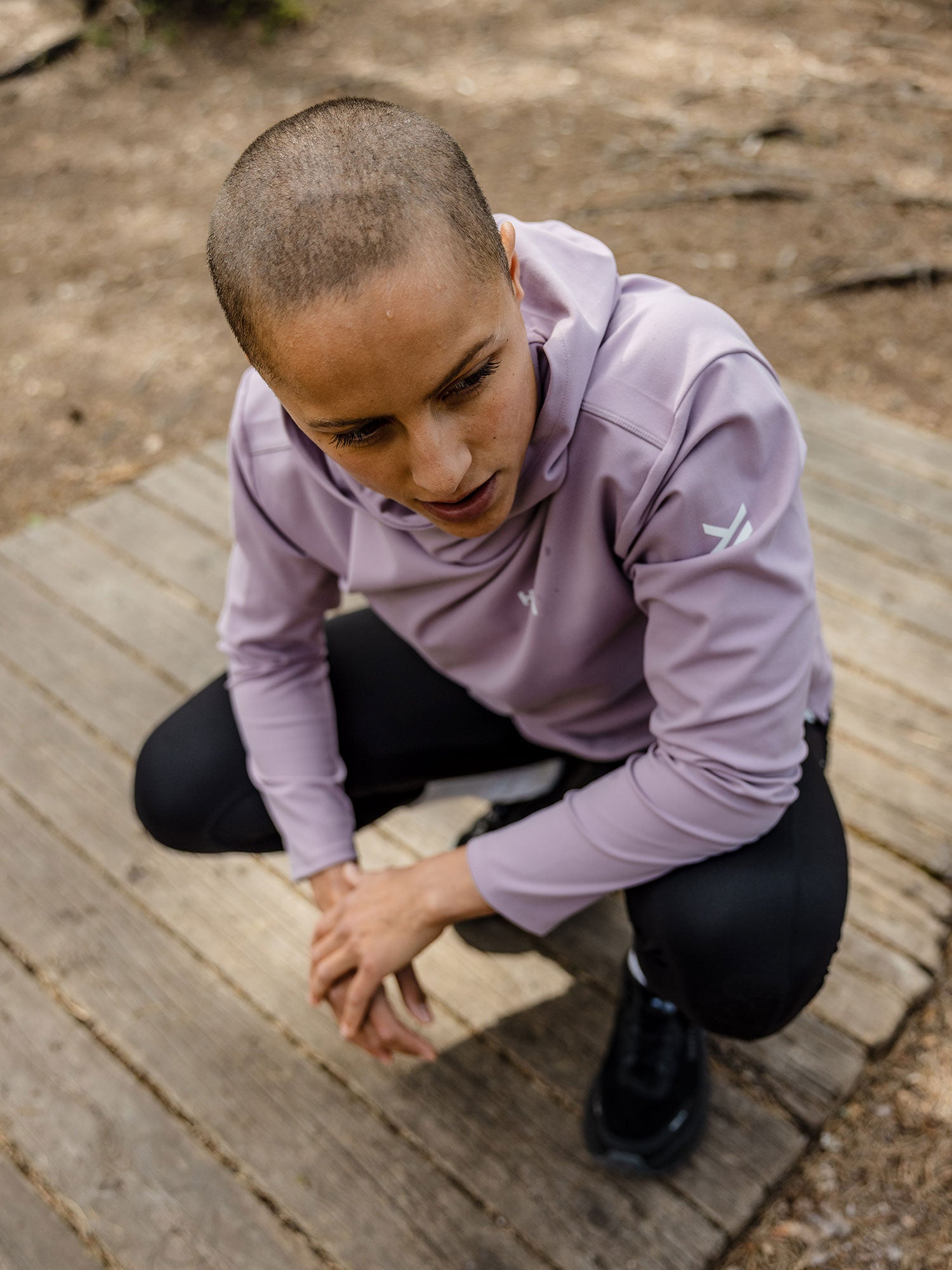 A person crouches outdoors on a wooden platform wearing a Halti Kaltio Training Hoodie Women's and black pants.