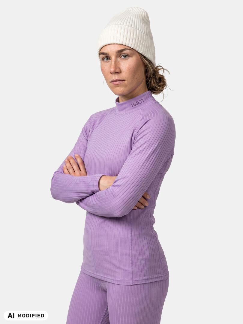 Woman wears Halti Dual Base Layer Set and white knit beanie, standing confidently with arms crossed, ready for adventure.