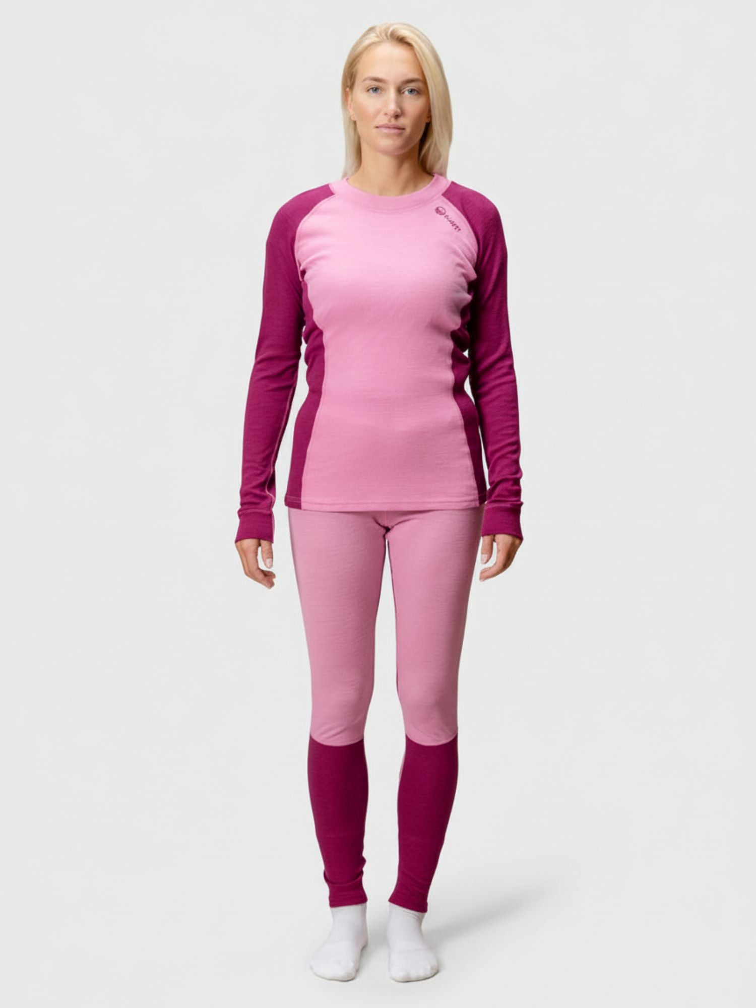 A woman models the Halti Hossa Merinowool Baselayer Set Women's in pink and burgundy, paired with white socks.