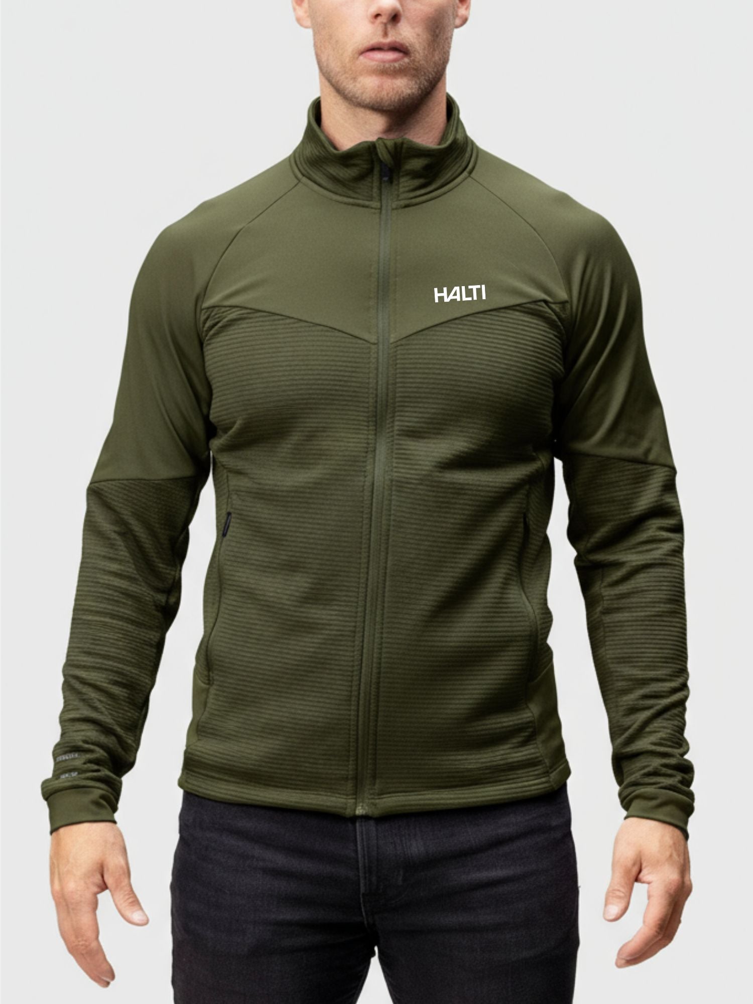 A man wears the Halti HeatGrid Layer Jacket, made from recycled polyester, standing against a plain background.