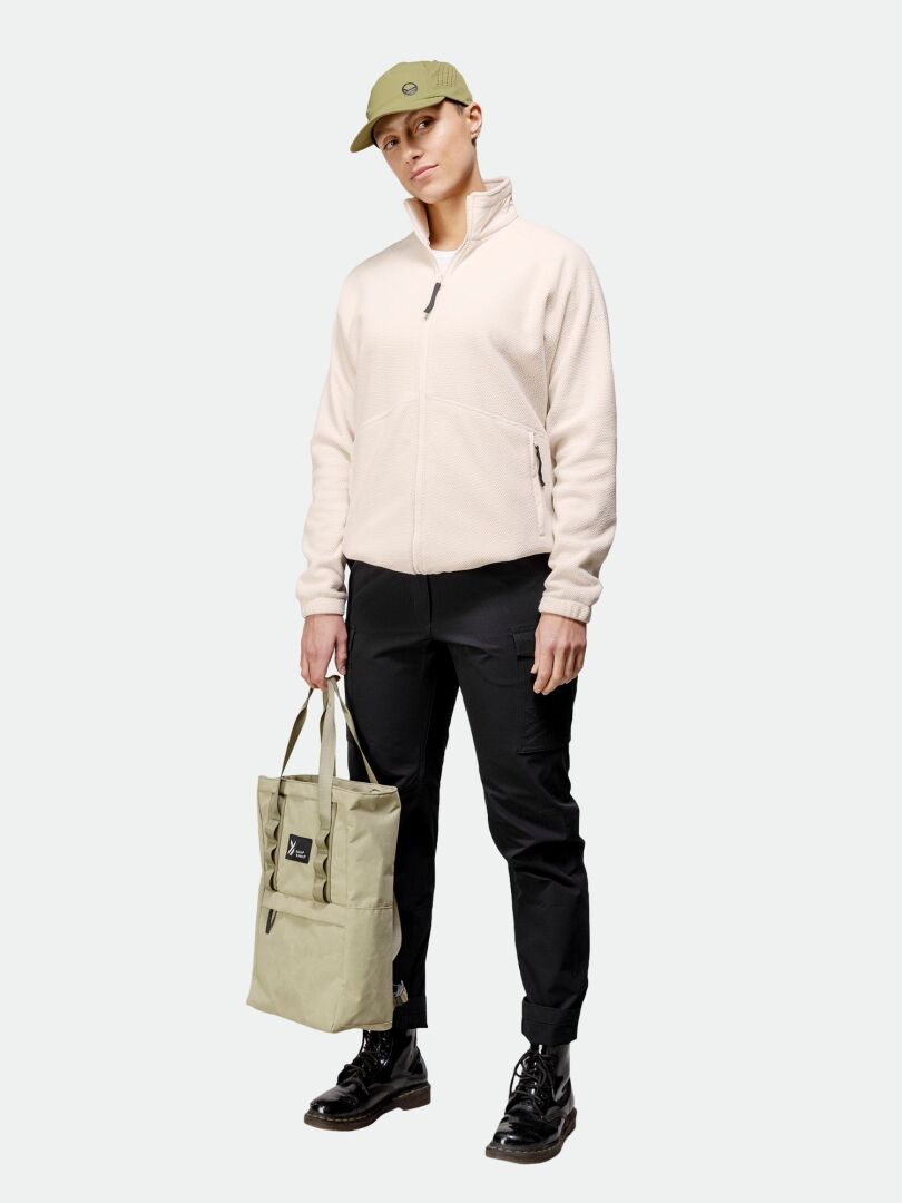 A woman wears the Halti Soolo Layer Jacket, black pants, green cap, and a light green tote bag, facing forward.