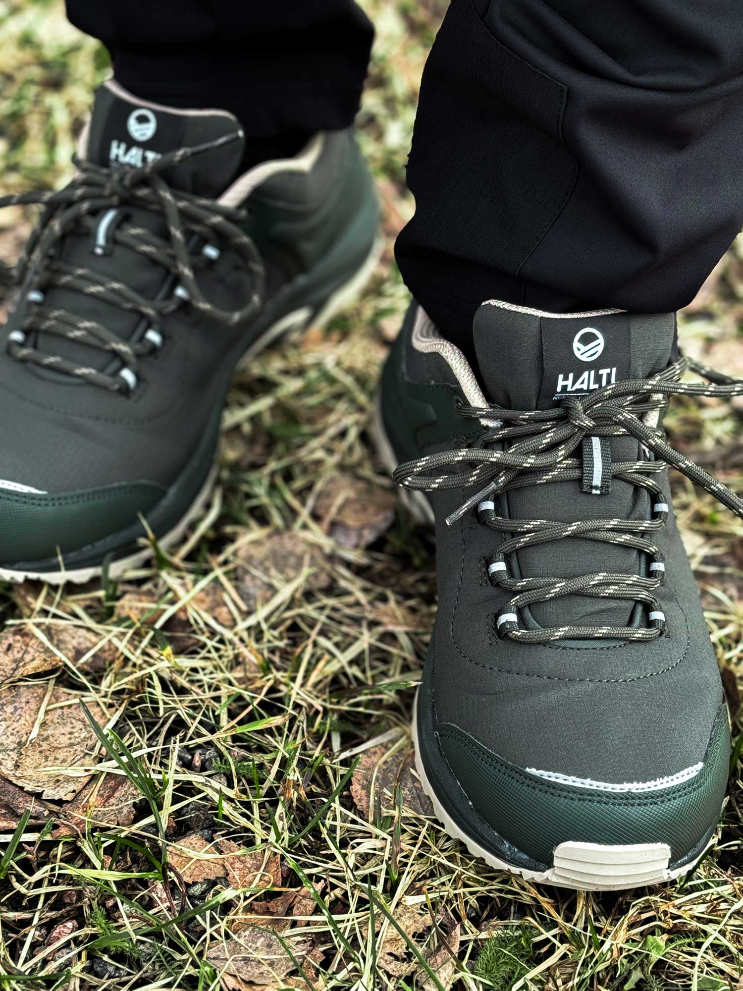Close-up of a person in Halti Outdoor Shoes Low DX Men's with GripmaxX Antislip sole, standing on grass and dry leaves.