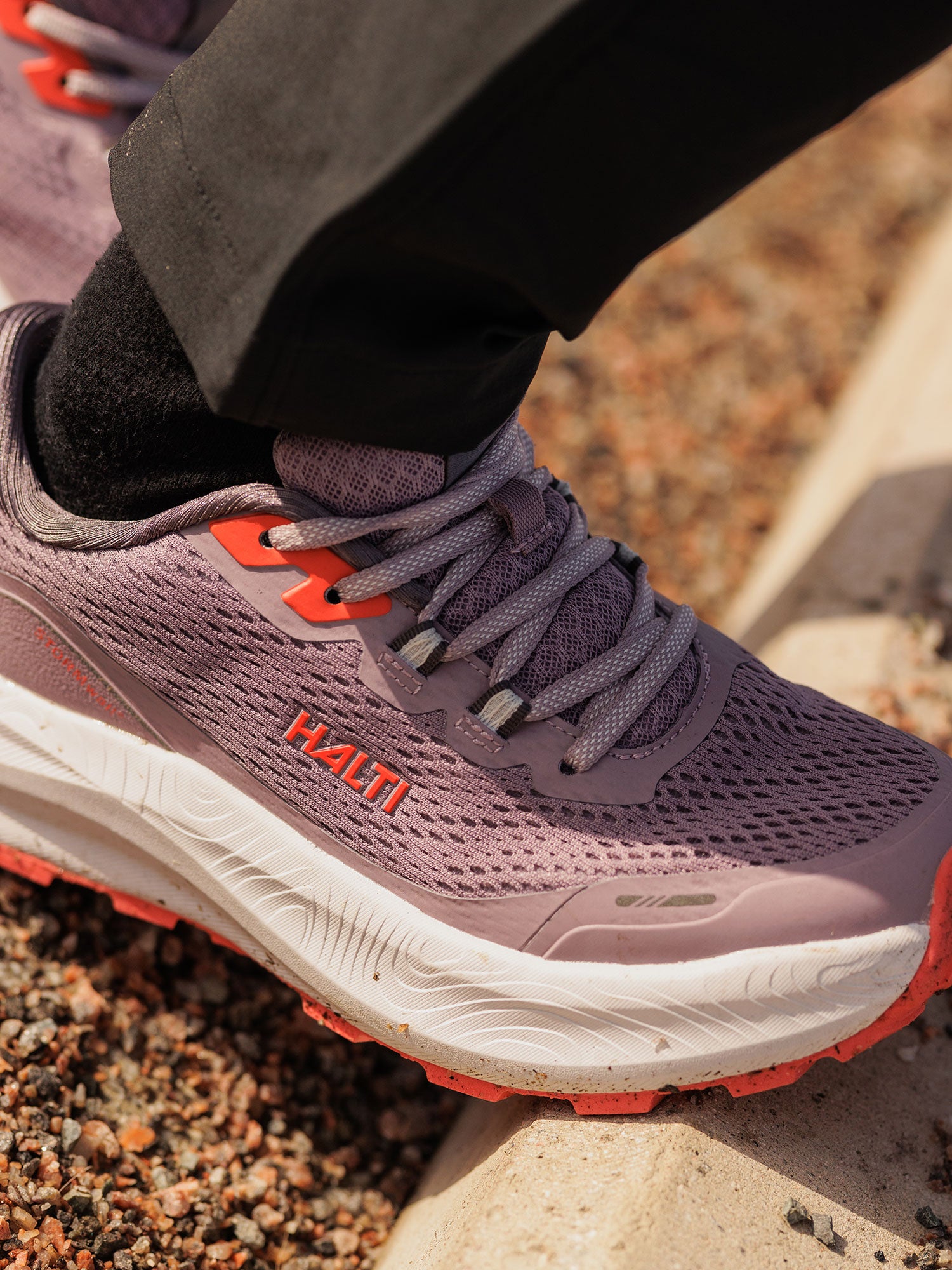 Close-up of a person in Halti Rapid 2 Sneaker Women's with cushioned Phylon midsole, standing on a curb by gravel.