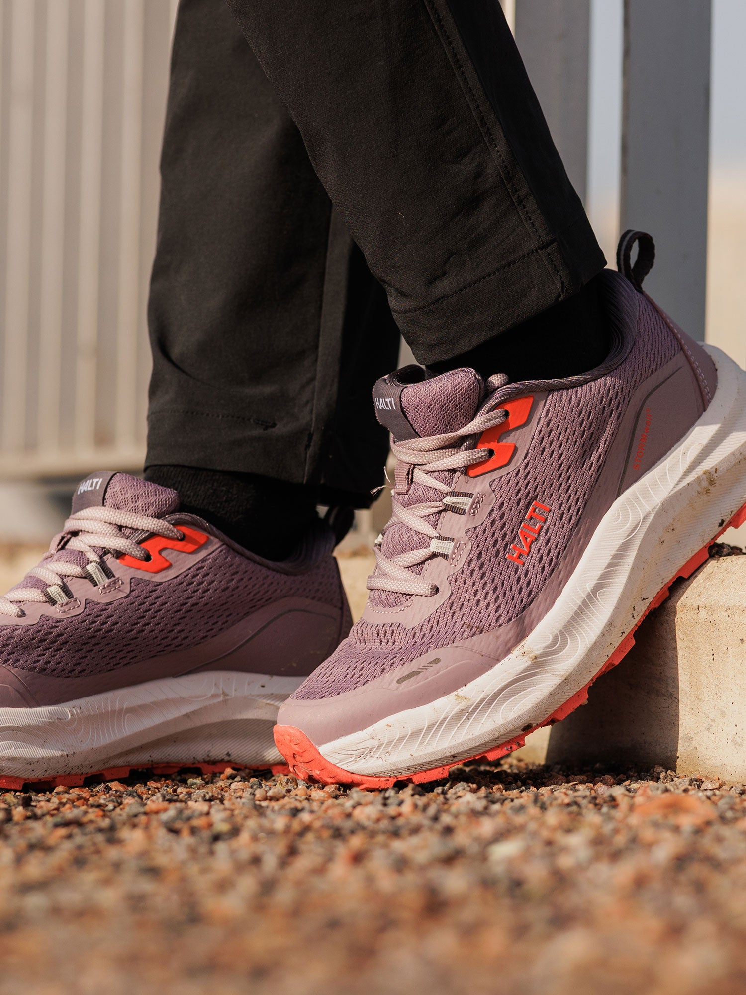 Person wearing Halti Rapid 2 Sneaker Women's with black pants, standing on gravel near a metal fence.