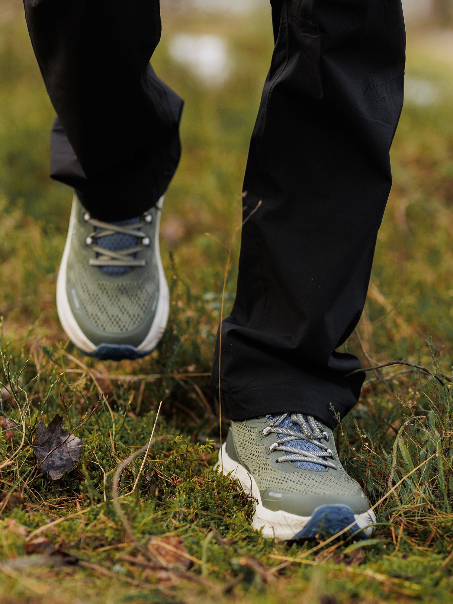 Person in black pants wearing Halti Rapid 2 Sneaker Men's, strolling on grass outdoors.